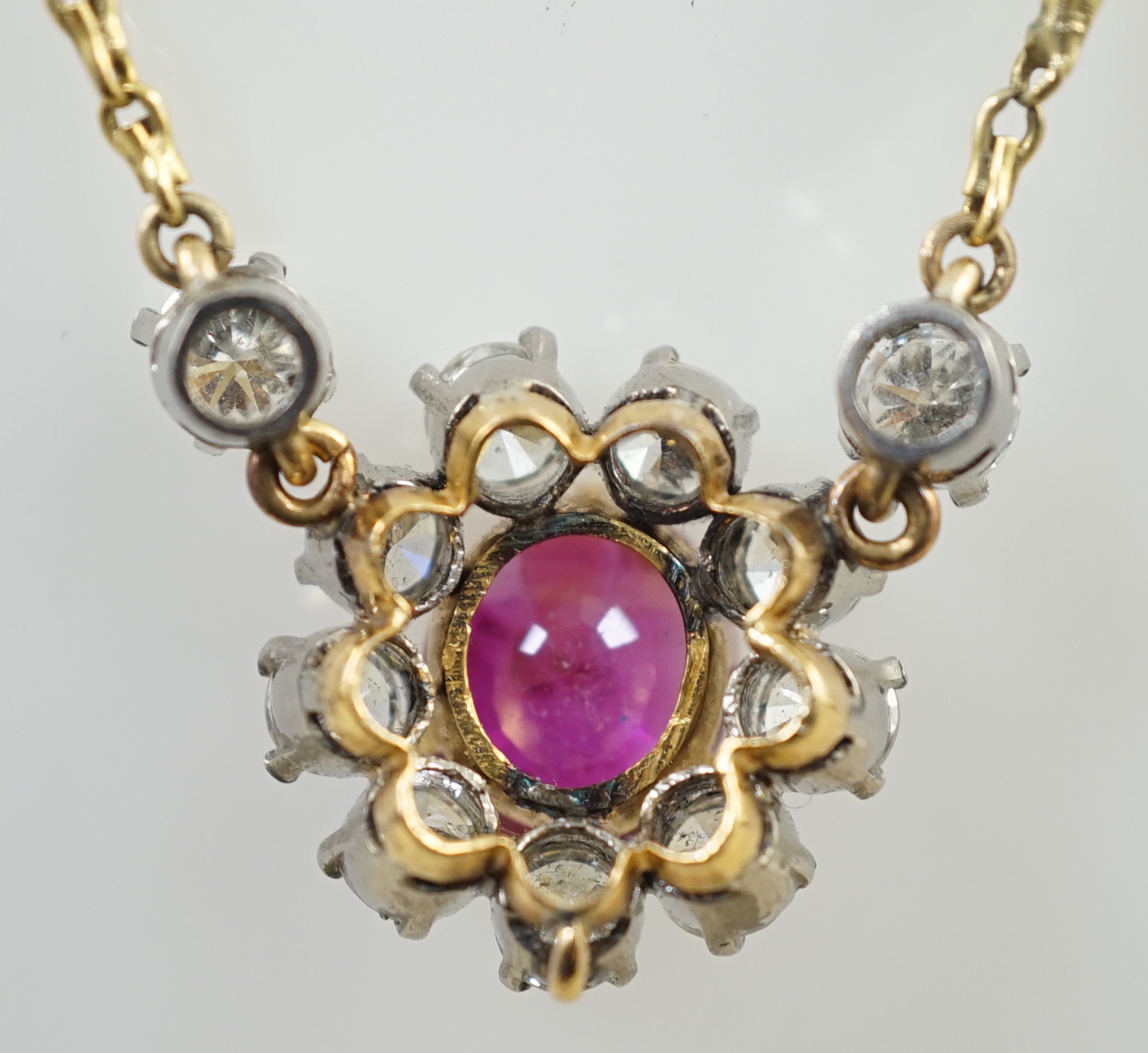 A modern 9ct gold, single stone oval cut ruby and eleven stone round cut diamond cluster set pendant necklace